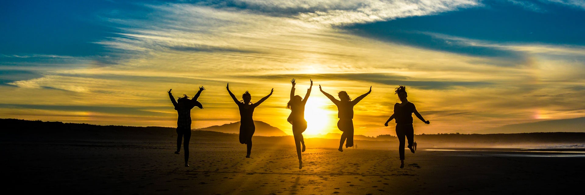 silhouettes of people running on a beach at sunset